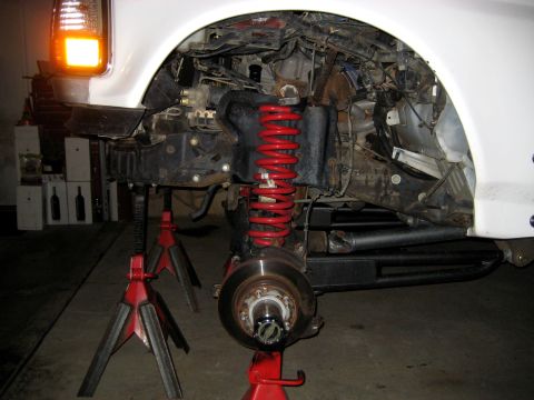 1996 Ford Bronco - Front suspension components, including a red coil spring and brake assembly, are visible with the vehicle supported by jack stands.