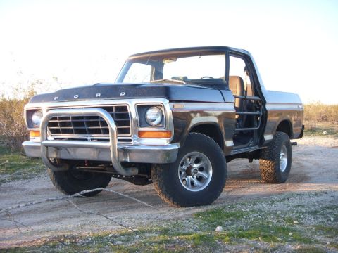 1978 Ford Bronco - Black full-size Ford Bronco with no top or doors, tube door bars and exposed roll bar, posed three-quarter front on a gravel pad with deser…