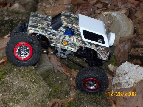 1978 Ford Bronco - This RC rock crawler features a camouflage body and white hardtop, navigating a rocky terrain.