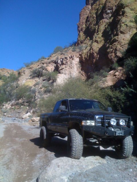 1966 Ford Bronco - A black Dodge Ram pickup truck navigates a , rocky terrain under a clear blue sky.