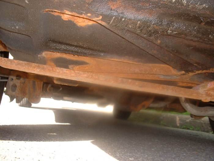 Underside of rusty car chassis, showing frame rails and suspension components