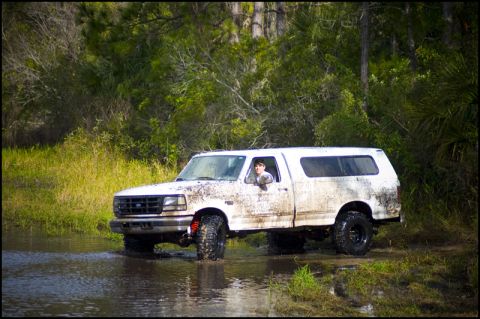 1996 Ford F-150 - A white Ford F-150 truck with a camper shell navigates through a muddy, watery terrain.