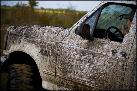 1996 Ford F-150 - Muddy 1996 Ford F-150 driving off-road, driver visible inside.