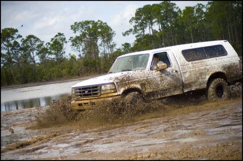 1996 Ford F-150 - A white 1996 Ford F-150 navigates a muddy off-road course, kicking up a large spray.