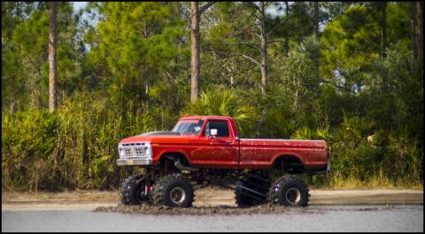 1996 Ford F-150 - This lifted pickup truck is equipped with oversized tires and appears to be driving through a muddy area.