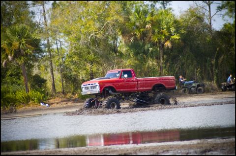 1996 Ford F-150 - A lifted red pickup truck is stuck in the mud while two ATVs are parked nearby.