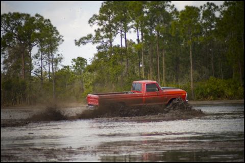 1996 Ford F-150 - A red pickup truck navigates a muddy terrain, creating a large splash.