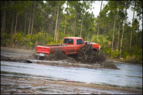 1996 Ford F-150 - A red 1979 Ford F-150 truck navigates a muddy off-road course, kicking up a large spray of dirt and water.