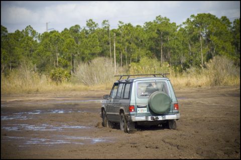 1996 Ford F-150 - SUV navigates a muddy terrain with a spare tire mounted on the rear and a roof rack overhead.