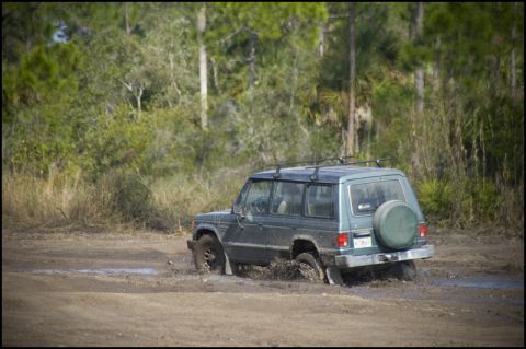 1996 Ford F-150 - This SUV is struggling to get through a muddy track, with trees in the background.