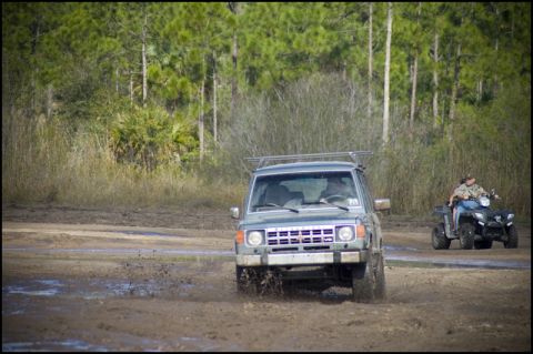 1996 Ford F-150 - An SUV navigates a muddy terrain with an ATV in the background.