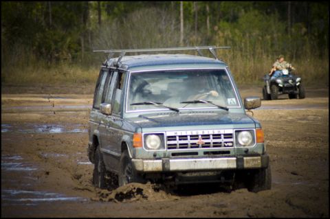 1996 Ford F-150 - A Mitsubishi Pajero navigates a muddy terrain, while an ATV follows behind in the distance.