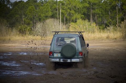 1996 Ford F-150 - SUV navigating a muddy trail, with trees and dry grass in the background.