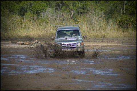 1996 Ford F-150 - A Mitsubishi Montero navigates a muddy terrain, creating a large splash.