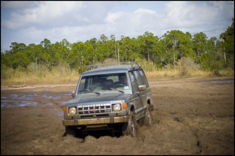 1996 Ford F-150 - A gray SUV navigates through a muddy terrain with trees in the background.