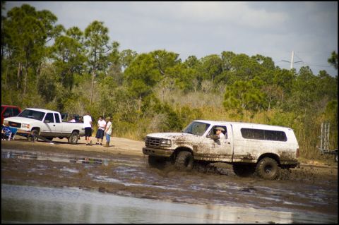 1996 Ford F-150 - A white Ford Bronco with a camper shell navigates a muddy track, kicking up water and mud.