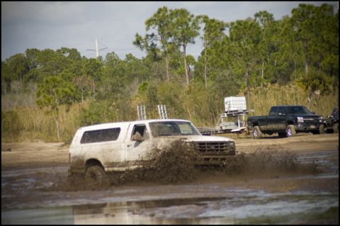 1996 Ford F-150 - White SUV driving through a mud pit with a black pickup truck visible behind it.