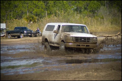 1996 Ford F-150 - A white Ford Bronco navigates a muddy track, kicking up water and dirt.