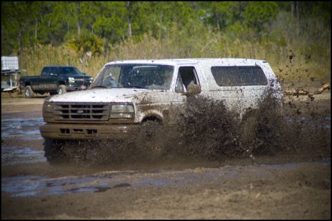 1996 Ford F-150 - A white SUV navigates a muddy track, kicking up a large spray of mud.