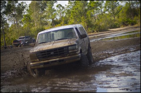 1996 Ford F-150 - A Ford Bronco navigates a muddy trail, kicking up water and mud.