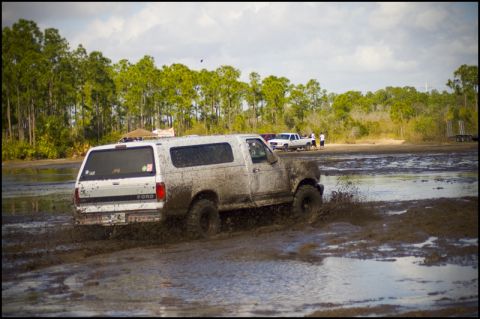 1996 Ford F-150 - A white Ford Bronco navigates a muddy terrain, kicking up water and mud.