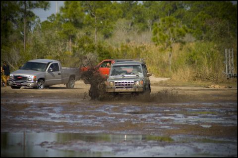 1996 Ford F-150 - Multiple off-road vehicles navigate a muddy track, creating large splashes.