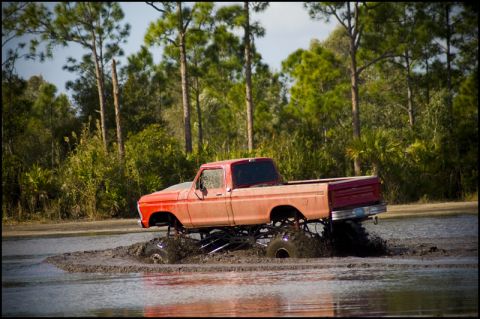 1996 Ford F-150 - A lifted red pickup truck navigates a muddy terrain with trees in the background.
