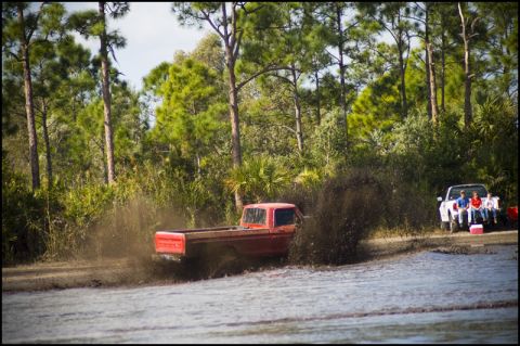 1996 Ford F-150 - A red 1979 Ford F-150 navigates a muddy track, while a white pickup truck and spectators observe from the side.