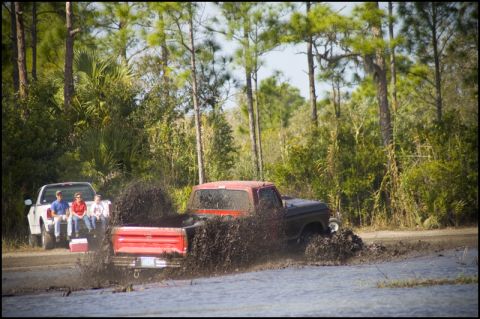1996 Ford F-150 - Two pickup trucks are seen in a muddy area with spectators in the background.