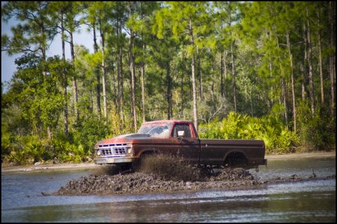1996 Ford F-150 - A classic 1977 Ford F-150 navigates a muddy off-road course, kicking up water and dirt.