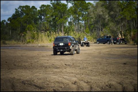 1996 Ford F-150 - Multiple off-road vehicles are present in a dirt lot with trees in the background.