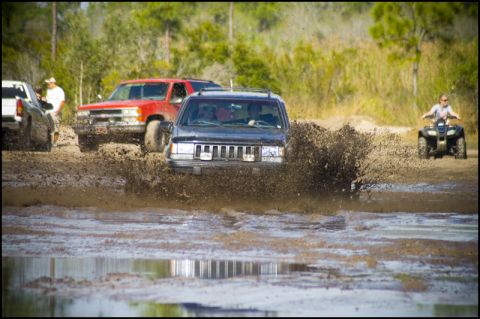 1996 Ford F-150 - Multiple off-road vehicles splash through a muddy track on a sunny day.