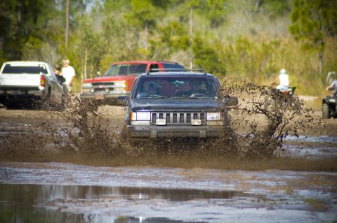 1996 Ford F-150 - Multiple vehicles navigating a muddy off-road course, with a Jeep Cherokee XJ creating a large splash.