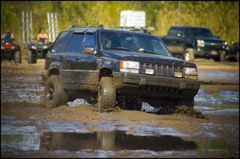 1996 Ford F-150 - A black Jeep Grand Cherokee navigates a muddy track, with other vehicles visible in the distance.