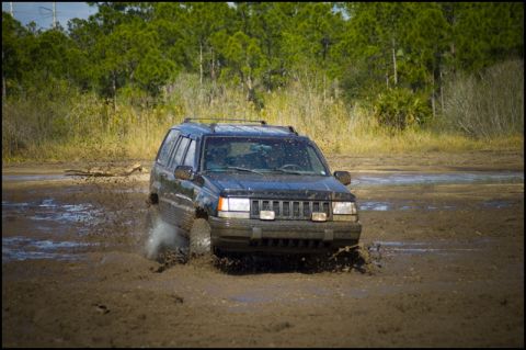 1996 Ford F-150 - Jeep Grand Cherokee navigates a muddy terrain, kicking up water and dirt.