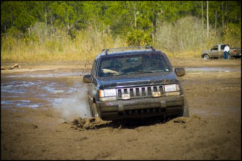 1996 Ford F-150 - A Jeep Grand Cherokee navigates through a muddy off-road course, with another vehicle visible in the distance.