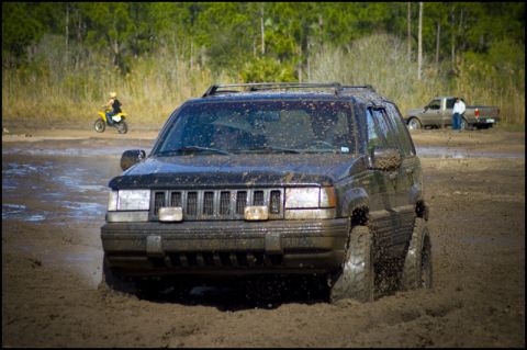 1996 Ford F-150 - A black Jeep Grand Cherokee is stuck in mud, with a dirt bike rider in the background.