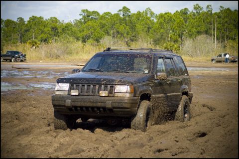 1996 Ford F-150 - A black 1996 Jeep Grand Cherokee navigates through a muddy off-road course, with other vehicles visible in the background.