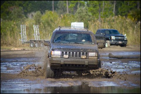 1996 Ford F-150 - A Jeep Grand Cherokee navigates a muddy track, kicking up water as it goes.