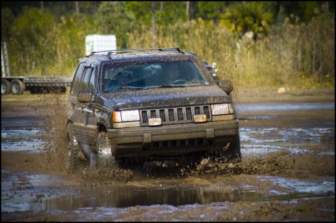 1996 Ford F-150 - A black Jeep Grand Cherokee navigates a muddy obstacle course, kicking up a significant amount of spray.