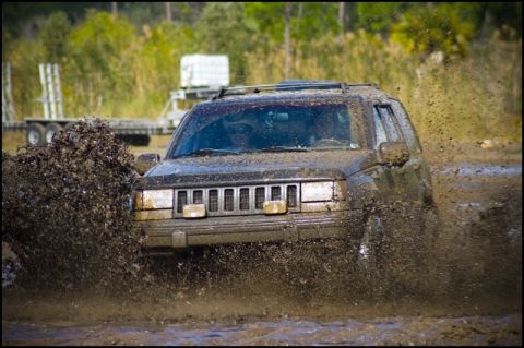 1996 Ford F-150 - Jeep Grand Cherokee navigates a muddy off-road course, kicking up a large spray.