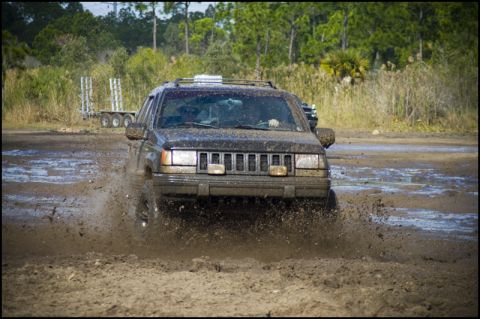 1996 Ford F-150 - A Jeep Grand Cherokee navigates a muddy track, sending spray into the air.