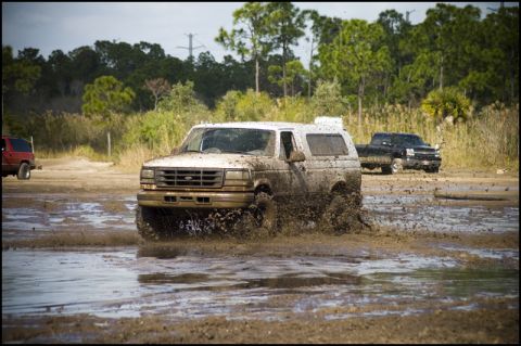 1996 Ford F-150 - A white 1996 Ford Bronco navigates a muddy track, kicking up water and dirt.