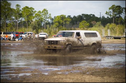 1996 Ford F-150 - White Ford Bronco driving through a mud bog, with spectators and other vehicles present.