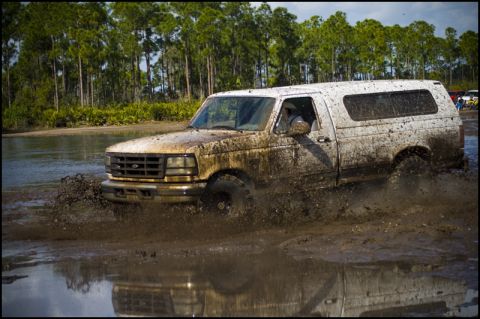 1996 Ford F-150 - A white Ford F-Series truck navigates through a muddy off-road course, kicking up water and mud.