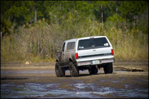 1996 Ford F-150 - This lifted Ford Bronco is navigating a muddy terrain, its off-road capabilities.