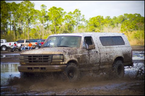 1996 Ford F-150 - Muddy 1996 Ford F-150 SUV splashing through a water obstacle with other vehicles visible.