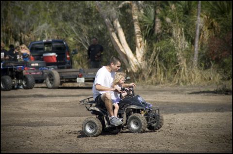 1996 Ford F-150 - A man and a young child ride an ATV on a dirt path, with other vehicles visible in the background.