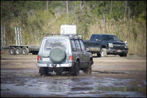 1996 Ford F-150 - Two off-road vehicles navigate a muddy terrain, kicking up water.