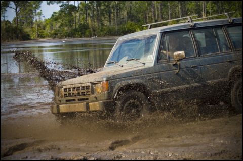 1996 Ford F-150 - An off-road vehicle navigates a muddy terrain, kicking up a large spray of water and dirt.